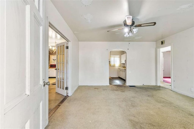 empty room featuring arched walkways, ceiling fan with notable chandelier, baseboards, and carpet