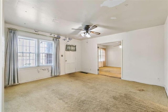 carpeted spare room with visible vents, baseboards, and ceiling fan