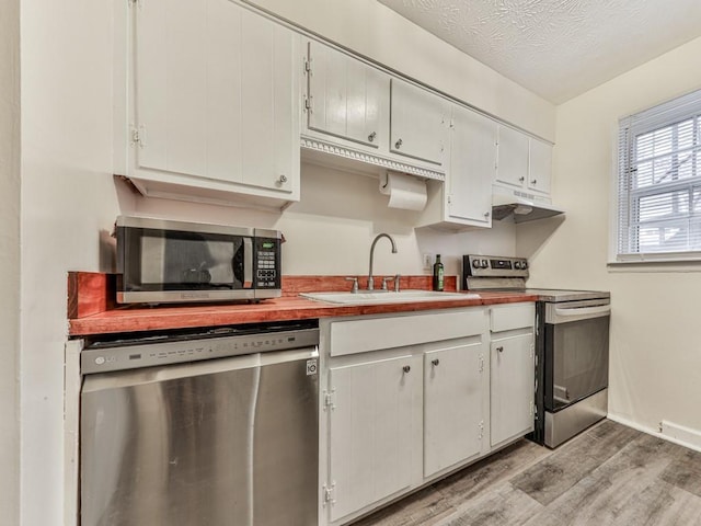 kitchen featuring appliances with stainless steel finishes, a sink, a textured ceiling, light wood-type flooring, and under cabinet range hood