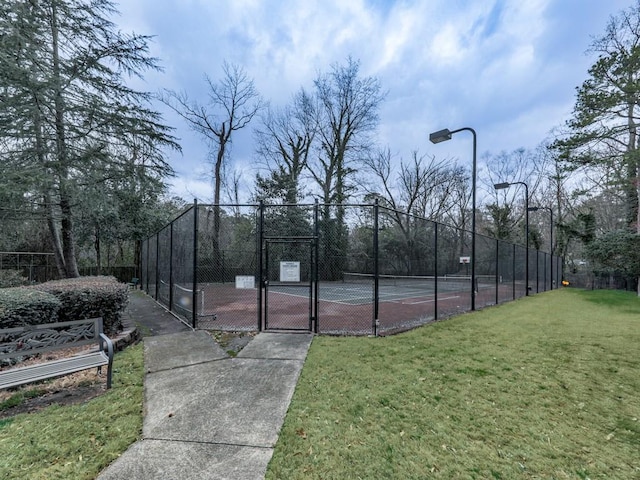 view of tennis court featuring a gate, fence, and a lawn