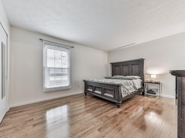 bedroom featuring a textured ceiling, light wood-style flooring, and baseboards