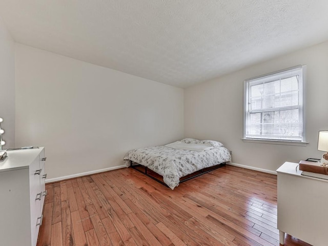 bedroom featuring light wood-style floors, a textured ceiling, and baseboards