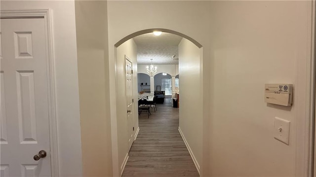 corridor with an inviting chandelier, baseboards, arched walkways, and dark wood-style flooring