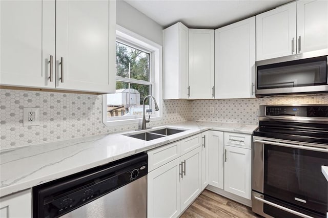 kitchen with stainless steel appliances, a sink, white cabinetry, light stone countertops, and tasteful backsplash