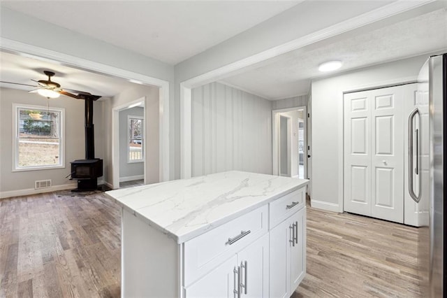 kitchen featuring visible vents, a wood stove, white cabinetry, light stone countertops, and stainless steel fridge