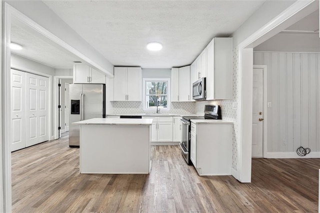 kitchen with white cabinets, appliances with stainless steel finishes, a center island, light countertops, and light wood-type flooring