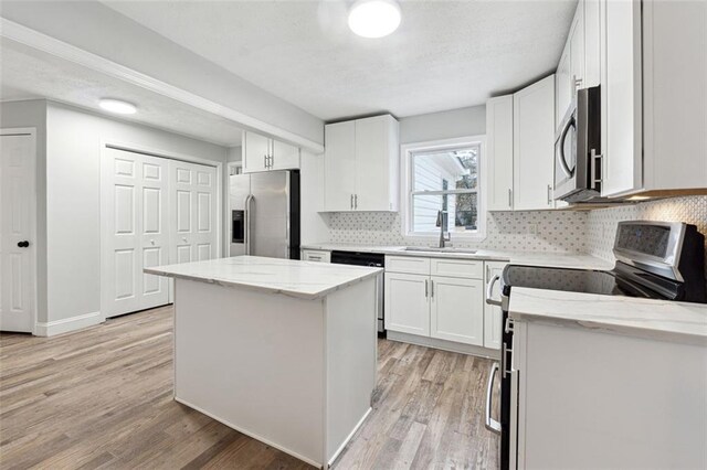 kitchen featuring stainless steel appliances, white cabinetry, a kitchen island, a sink, and light stone countertops