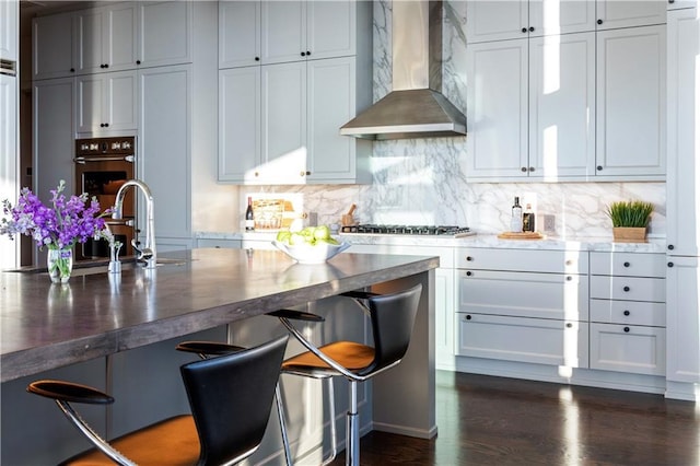 kitchen with stainless steel gas stovetop, sink, dark hardwood / wood-style flooring, decorative backsplash, and wall chimney exhaust hood