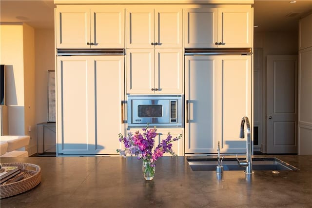 kitchen with built in appliances, concrete flooring, sink, and white cabinets