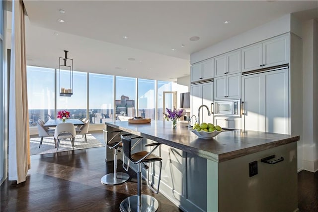 kitchen featuring dark hardwood / wood-style floors, sink, built in appliances, floor to ceiling windows, and a center island with sink