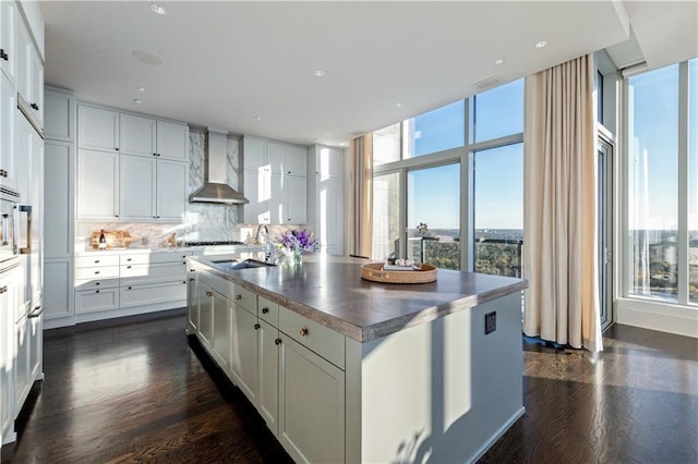 kitchen with white cabinetry, a healthy amount of sunlight, wall chimney exhaust hood, and a kitchen island with sink