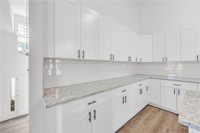 kitchen with light hardwood / wood-style floors, white cabinetry, light stone counters, and tasteful backsplash