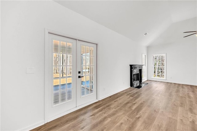 unfurnished living room featuring light hardwood / wood-style floors, vaulted ceiling, a high end fireplace, ceiling fan, and french doors