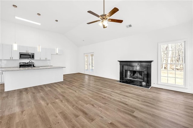 unfurnished living room featuring ceiling fan, light hardwood / wood-style flooring, a premium fireplace, and high vaulted ceiling