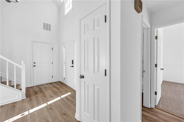 hall featuring light wood-type flooring and a towering ceiling