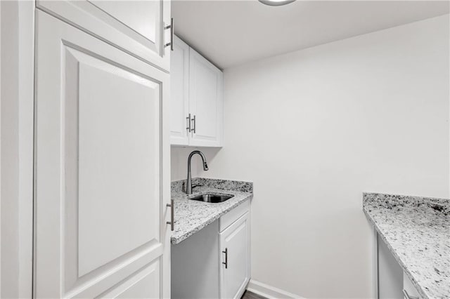 kitchen featuring white cabinets, light stone counters, and sink