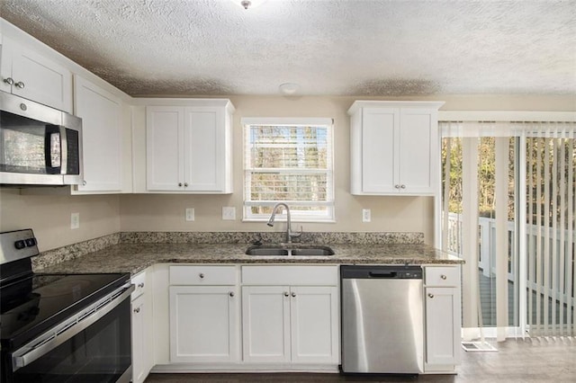 kitchen with appliances with stainless steel finishes, sink, white cabinetry, and dark stone counters