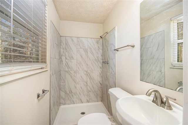 bathroom featuring a textured ceiling, toilet, tiled shower, and sink