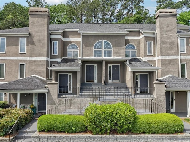 view of front of home featuring a shingled roof, stucco siding, and a chimney