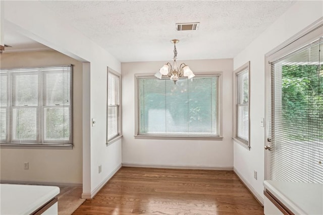 unfurnished dining area featuring visible vents, wood finished floors, baseboards, a textured ceiling, and a chandelier