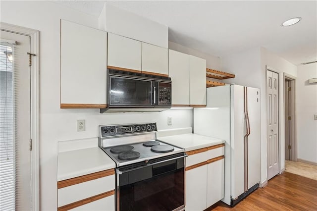 kitchen with electric range, black microwave, light countertops, freestanding refrigerator, and white cabinetry