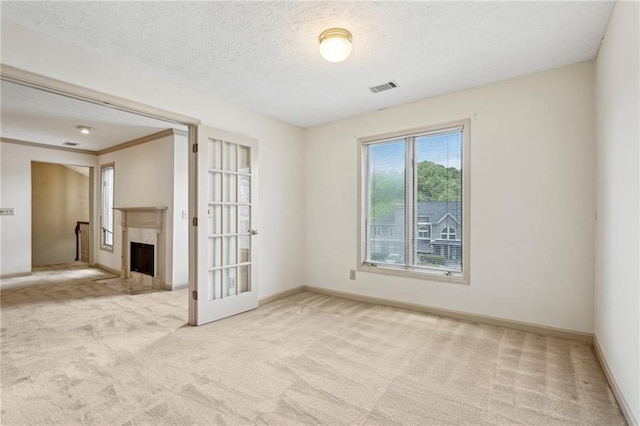 carpeted spare room with a premium fireplace, a textured ceiling, baseboards, and visible vents
