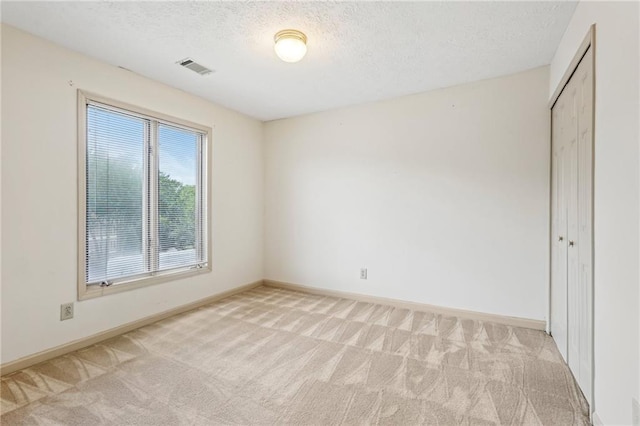 unfurnished room featuring a textured ceiling, light colored carpet, baseboards, and visible vents