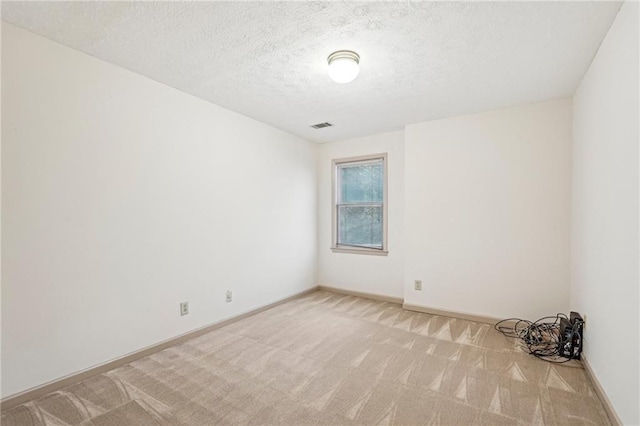 unfurnished room with a textured ceiling, light colored carpet, baseboards, and visible vents