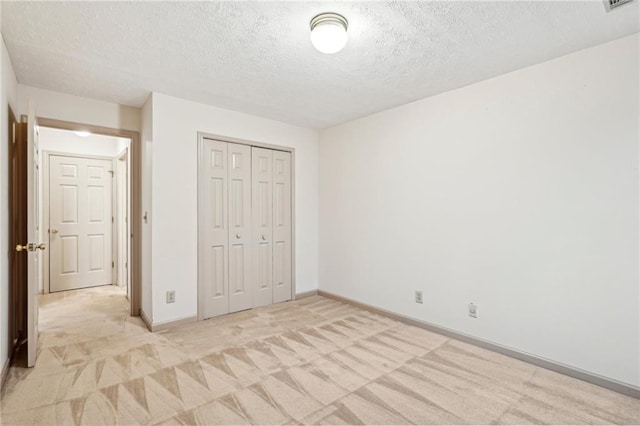 unfurnished bedroom with a textured ceiling, visible vents, baseboards, a closet, and light carpet