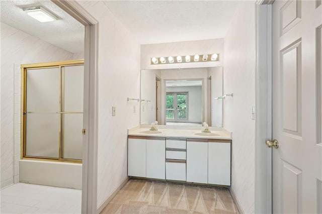 bathroom featuring double vanity, a sink, a textured ceiling, and enclosed tub / shower combo