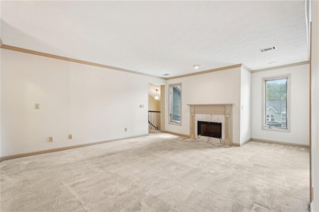 unfurnished living room with crown molding, carpet flooring, a premium fireplace, baseboards, and visible vents