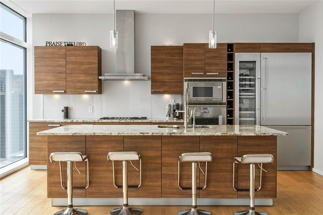 kitchen featuring built in appliances, a center island with sink, light stone countertops, and light hardwood / wood-style floors