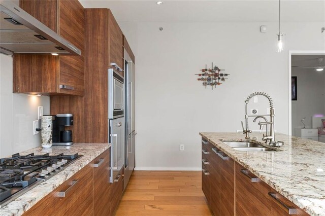 kitchen featuring pendant lighting, light hardwood / wood-style flooring, stainless steel gas cooktop, sink, and light stone counters