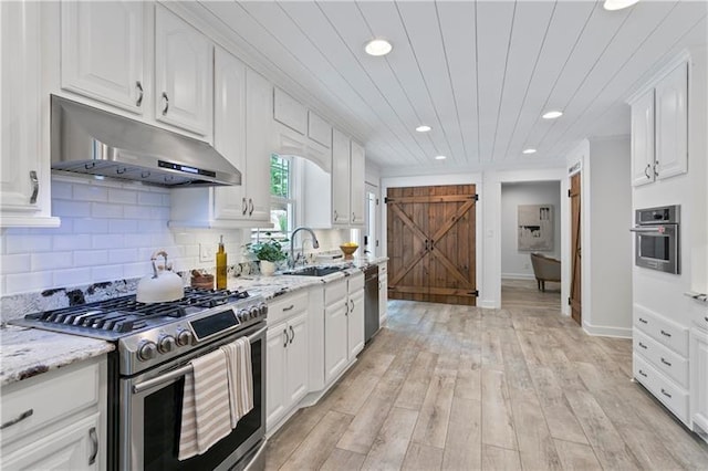 kitchen with sink, appliances with stainless steel finishes, light stone counters, white cabinets, and a barn door