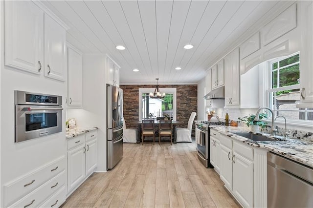 kitchen with sink, appliances with stainless steel finishes, white cabinetry, light stone counters, and decorative light fixtures