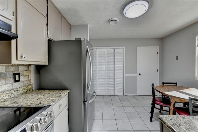 kitchen with light stone countertops, stainless steel appliances, backsplash, and light tile patterned floors