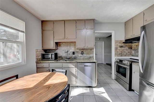 kitchen with decorative backsplash, light tile patterned floors, light stone countertops, sink, and stainless steel appliances