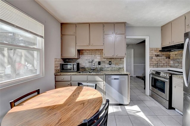 kitchen with cream cabinets, light tile patterned floors, appliances with stainless steel finishes, light stone counters, and tasteful backsplash