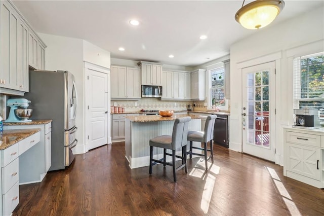 kitchen featuring a center island, dark hardwood / wood-style floors, light stone countertops, tasteful backsplash, and stainless steel appliances