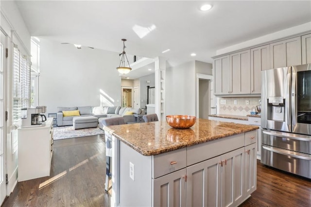 kitchen with light stone countertops, dark wood-type flooring, stainless steel fridge with ice dispenser, decorative backsplash, and a kitchen island