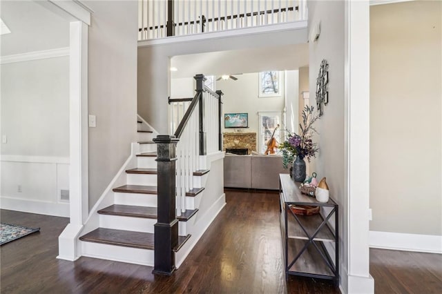 foyer entrance with a fireplace, a towering ceiling, dark hardwood / wood-style floors, and crown molding