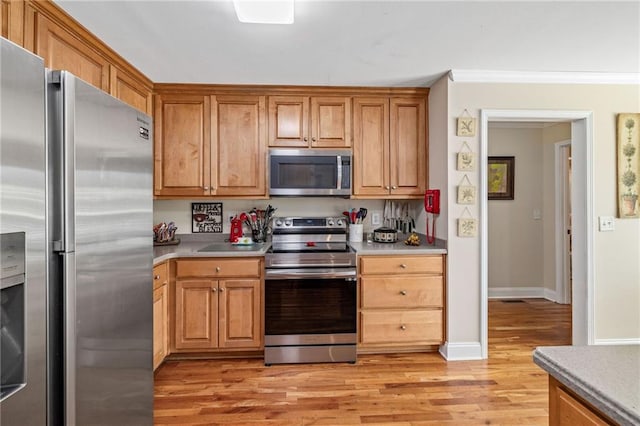 kitchen with light countertops, crown molding, baseboards, appliances with stainless steel finishes, and light wood-type flooring