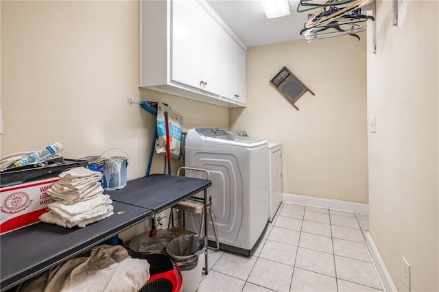 clothes washing area with baseboards, washer and dryer, cabinet space, and light tile patterned floors