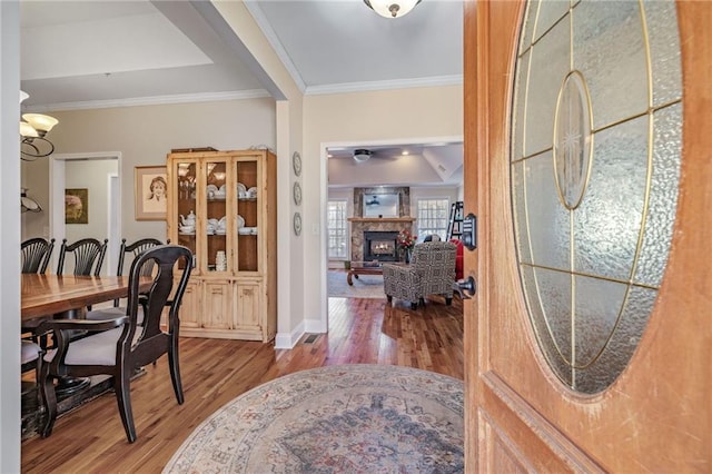 foyer entrance featuring ornamental molding, baseboards, a ceiling fan, a glass covered fireplace, and wood finished floors