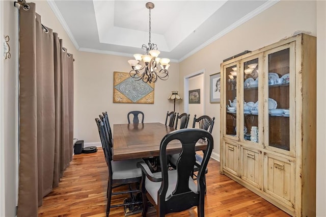 dining space featuring baseboards, ornamental molding, light wood-style floors, a tray ceiling, and a notable chandelier