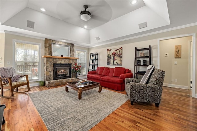 living area featuring a tray ceiling, crown molding, a stone fireplace, ceiling fan, and hardwood / wood-style floors