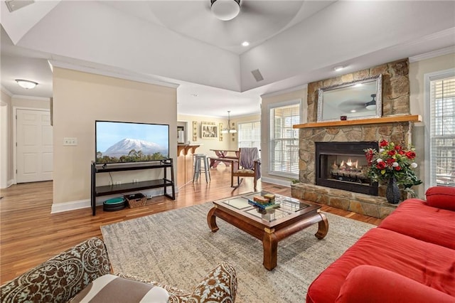 living room with crown molding, baseboards, a ceiling fan, a stone fireplace, and wood finished floors
