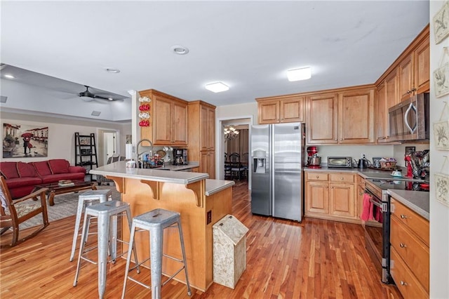 kitchen with open floor plan, a kitchen bar, stainless steel appliances, light wood finished floors, and a peninsula