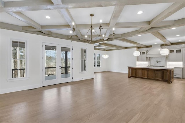 unfurnished living room with hardwood / wood-style floors, beamed ceiling, coffered ceiling, an inviting chandelier, and french doors