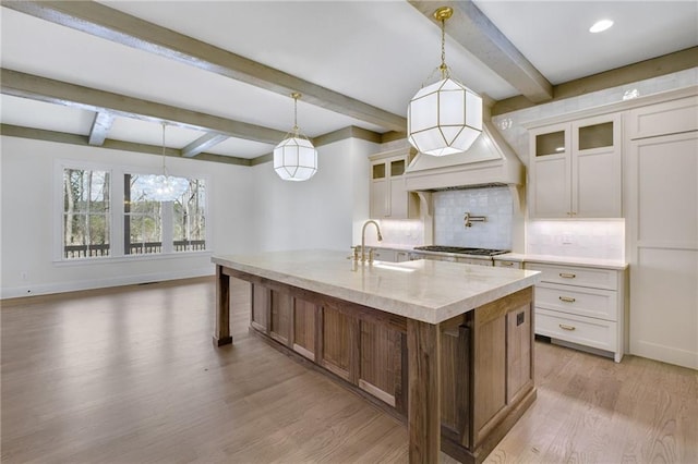 kitchen featuring sink, decorative light fixtures, white cabinets, and a center island with sink